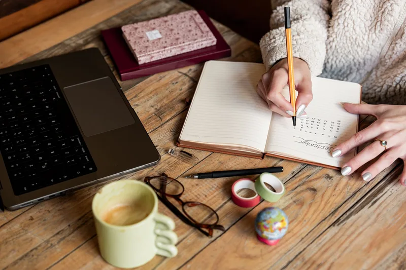 Woman planning her part-time work schedule in a notebook beside her laptop and coffee