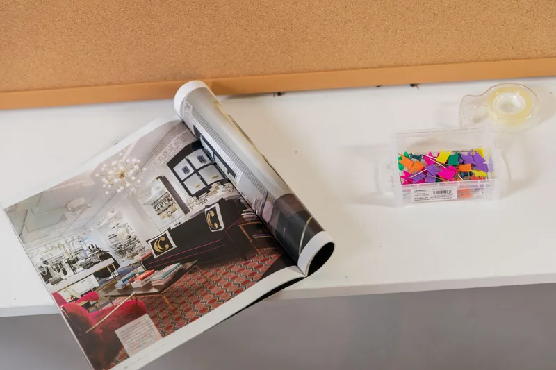 An overhead view of a workspace with a magazine, colorful pins, and design materials, evoking a Pinterest content workflow