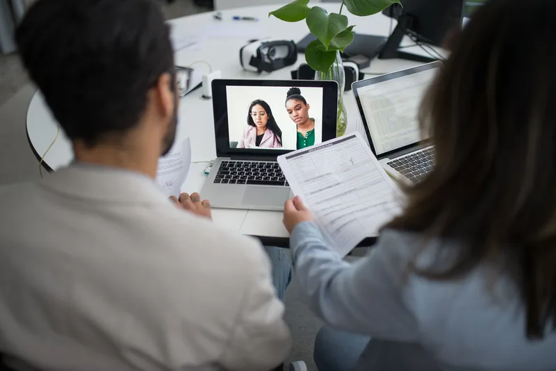 Two professionals in a virtual hiring interview using laptops in an office setting