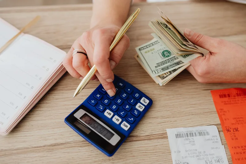 Hands using a calculator with cash and receipts, representing startup cost planning for a new VA business