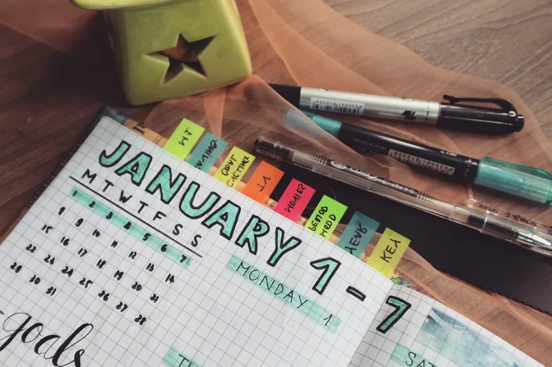Detailed planner with colorful tabs and pens on a wooden desk, representing milestone tracking for a new business