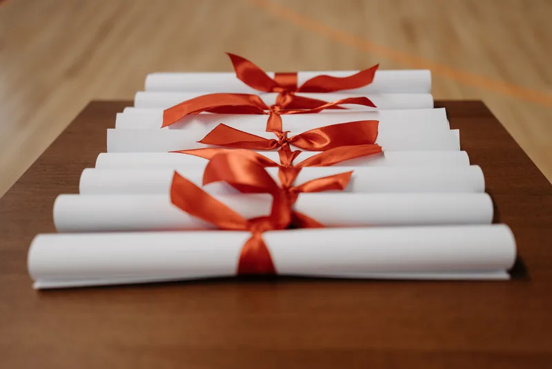 A stack of rolled certificates tied with ribbon on a table, representing the physical credential a paid VA certification program provides