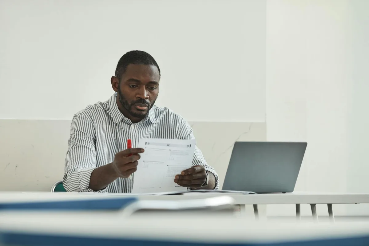 Business owner comparing two VA test project outputs on their laptop, notepad with evaluation criteria beside them