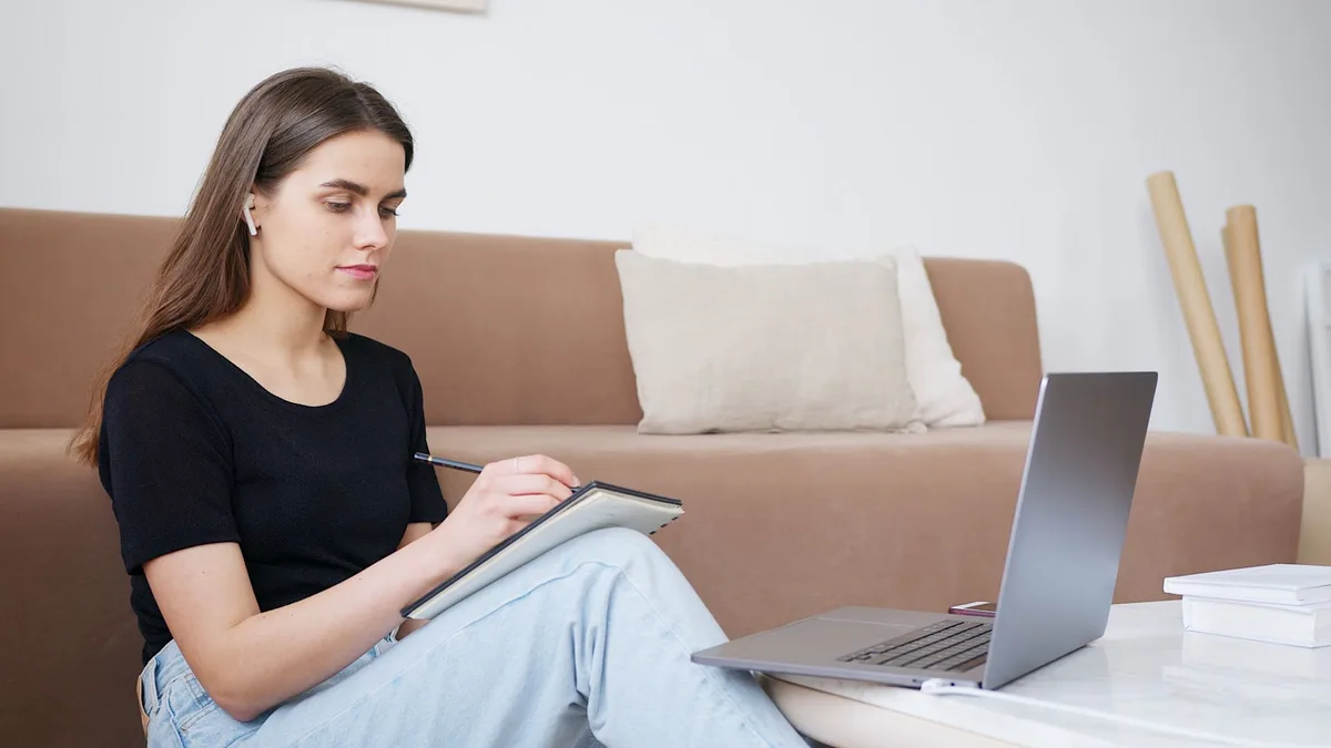 Glad young woman in a cozy living room writing down notes while attending an online interview