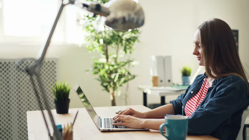 A woman smiling while working on a laptop in a home office