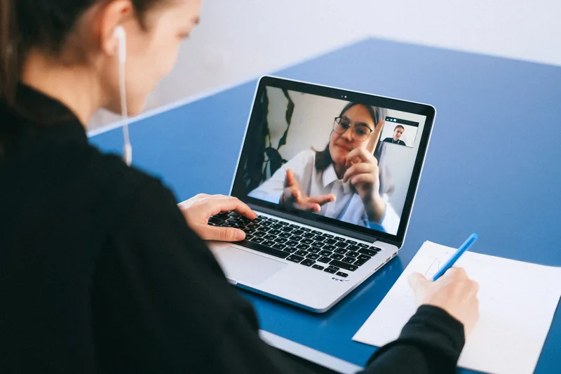 A woman on a video call with notes and a laptop, working remotely