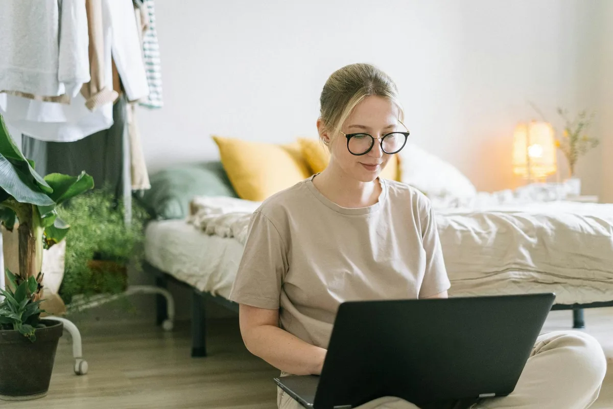 Woman working at a bright home office desk with a laptop and coffee, natural light from a window